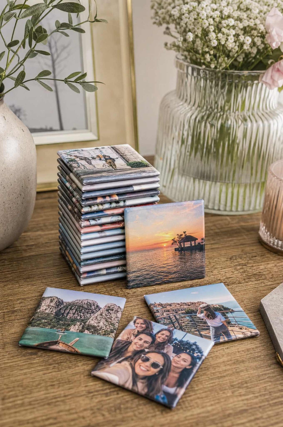 A stack of 2x2 photo magnets on a wooden table with a few fanned out, beach and city photos