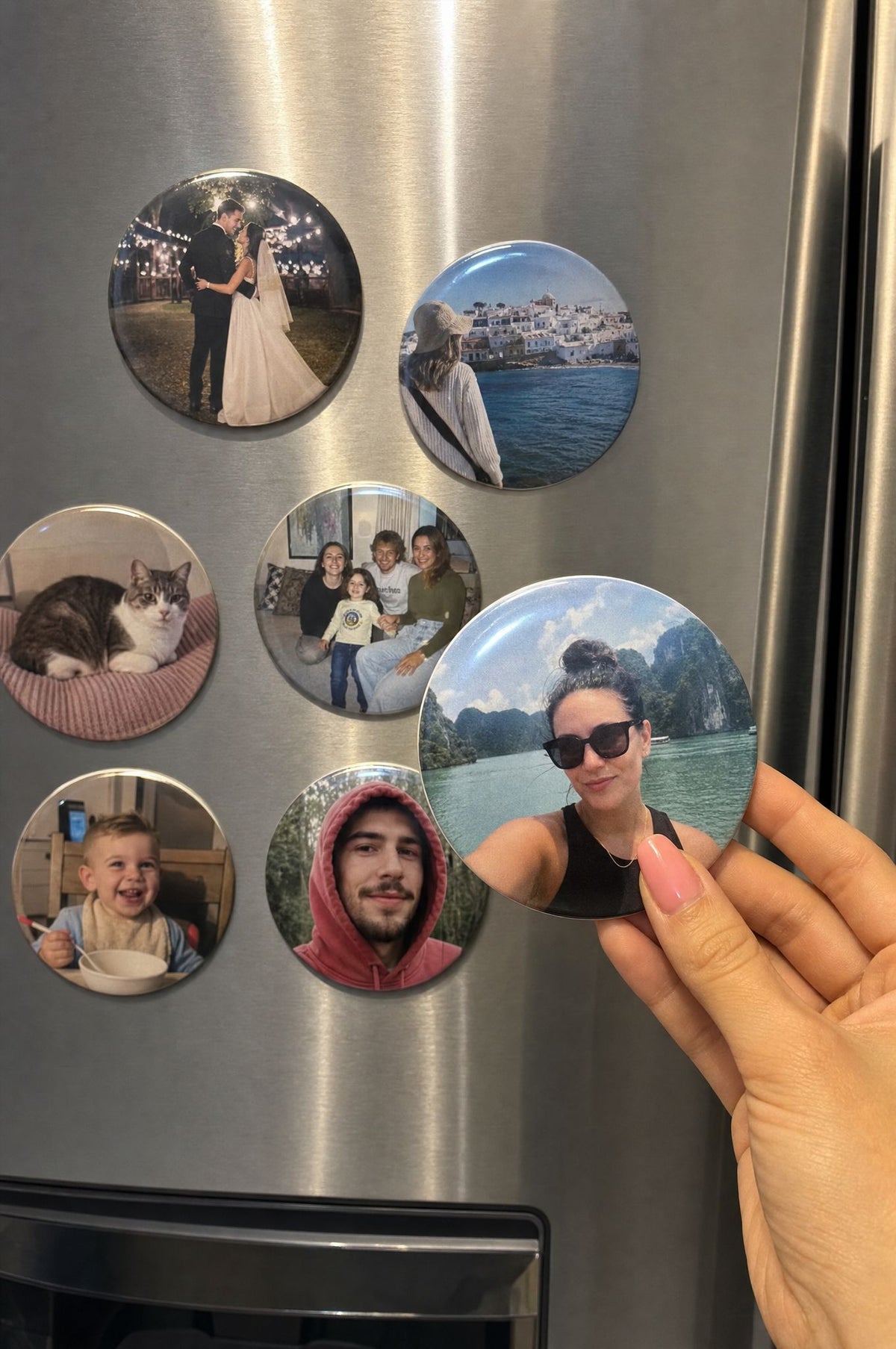 3 inch round photo magnets on a stainless steel fridge, a hand placing one with a couple photo
