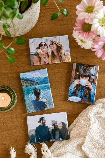 2x3 rectangle photo magnets scattered on a wooden table with flowers and a candle, couple and travel photos