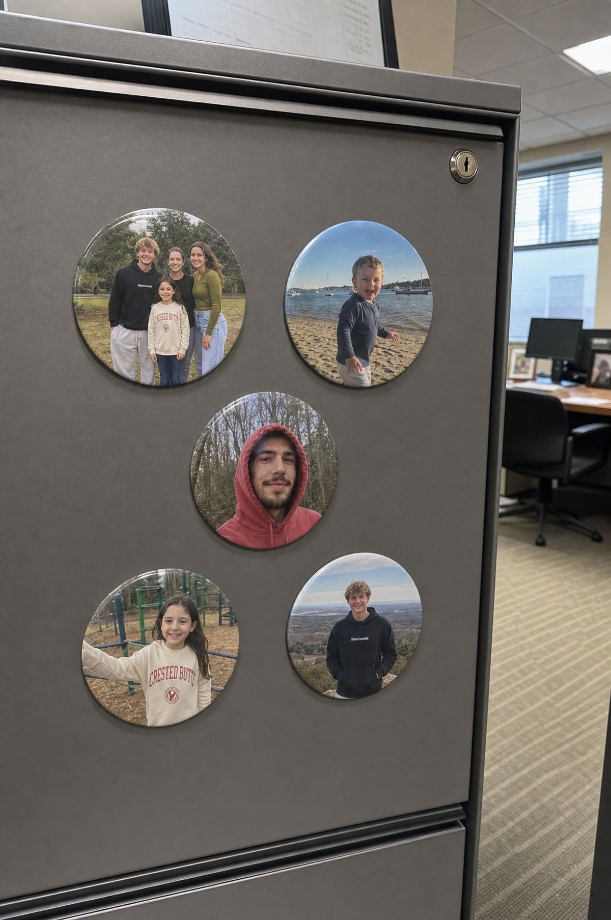 Six 3 inch round photo magnets on a grey metal office cabinet, portraits of coworkers